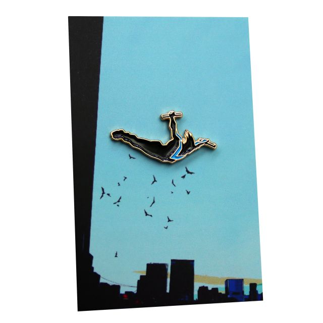 A custom pin badge of DC Comics character, Nightwing, diving off a building. The backingcard features a cityscape of Gotham City.