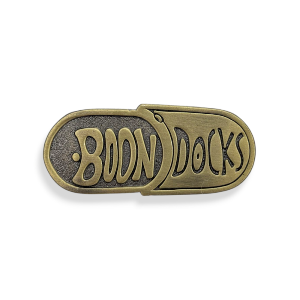 An antique gold die struck badge in the shape of a pill with the words Boon Docks on the front.