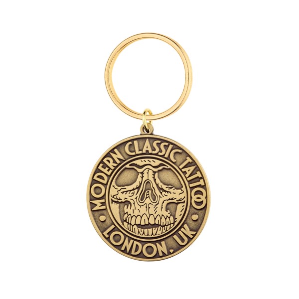 A circle metal keyring in a gold antiqued gold plating with a tattoo skull on the front.
