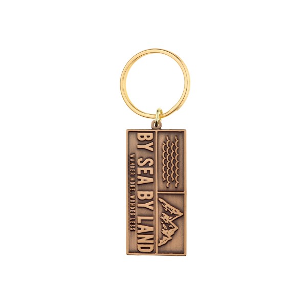 A rectangular metal keychain in a bronze-effect plating. The design says By Sea and By Land and has line drawings of the ocean and mountains on it.