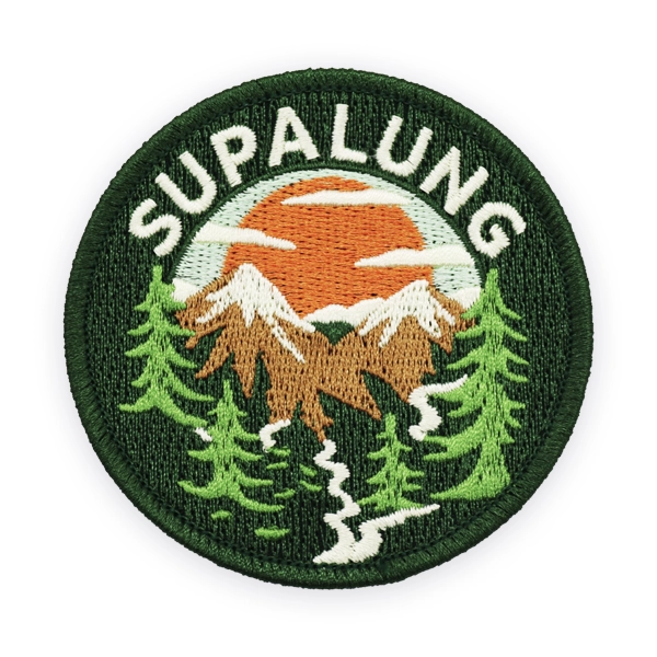 Round embroidered patch showing mountains, pine trees and a winding path under an orange sky, stitched in green and brown thread, ideal as a custom embroidered patch for outdoor, hiking or nature themed embroidered patches.