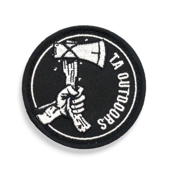 A black circular patch featuring a hand holding an axe with the words TA Outdoors down the side.