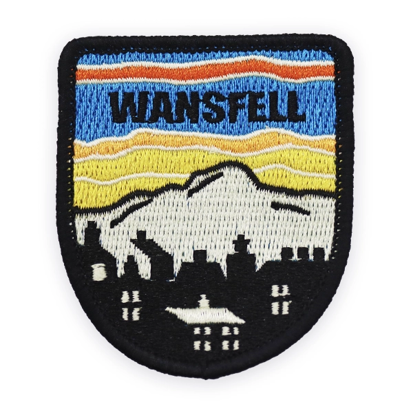 Shield shaped embroidered patch showing layered hills, skyline and “Wansfell” text in blue, yellow and black thread, designed as a custom embroidered patch for walking, hiking and countryside embroidered patches.