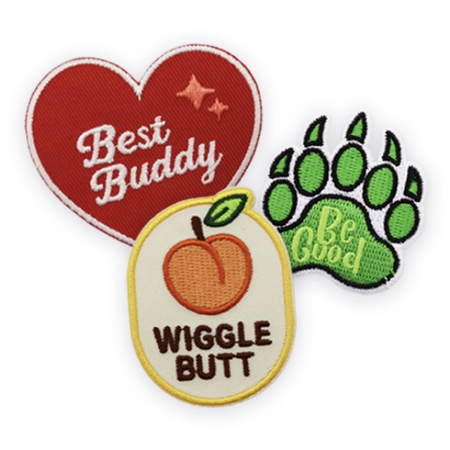 Set of custom patches showing dog themed embroidered designs including a red heart reading “Best Buddy”, a green paw print with “Be Good”, and a peach “Wiggle Butt” patch, stitched as playful custom patches UK for pet accessories or gifts.