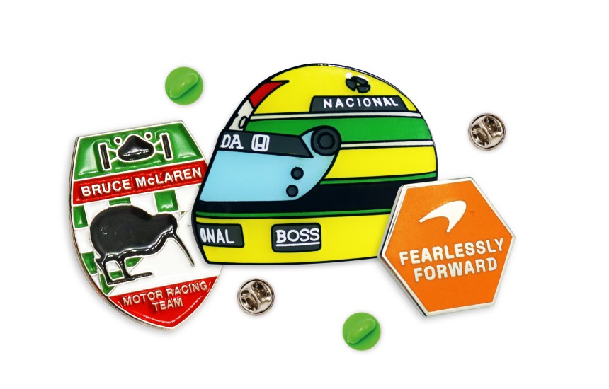 F1 Custom Merch - An Aryton Senna vintage f1 helmet pin badge, a Bruce McLaren long service award badge, and McLaren's Fearlessly Forward branding enamel pin.