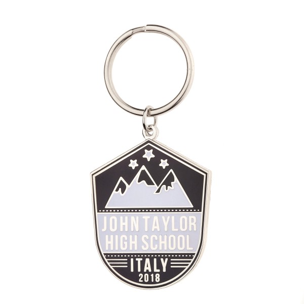 A shield-shaped custom enamel keyring with a black background, white mountains, and the words