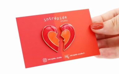 A broken heart pin badge attached to a vibrant red backing card.