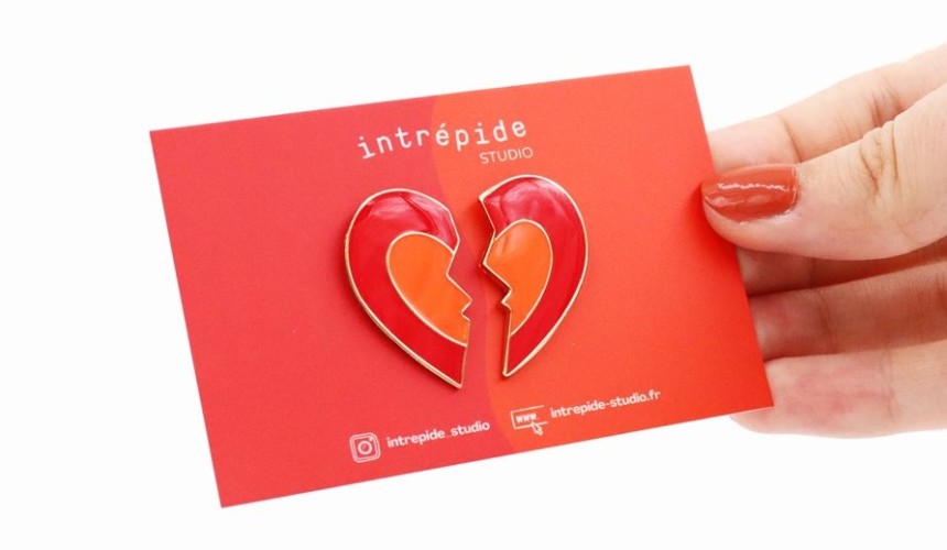 A broken heart pin badge attached to a vibrant red backing card.