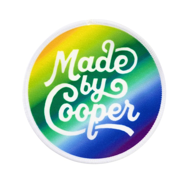 Printed patch with a rainbow colour gradient and the Made by Cooper logo in white.