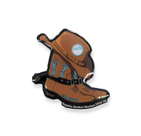 A printed pin badge of a cowboy hat resting on a brown cowboy boot.