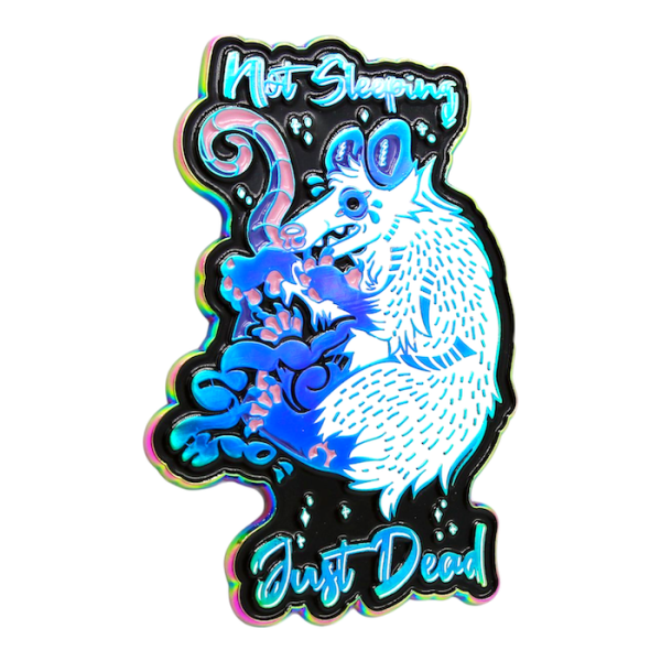 A pin badge of a nasty looking possum sleeping. The texts around the badge reads