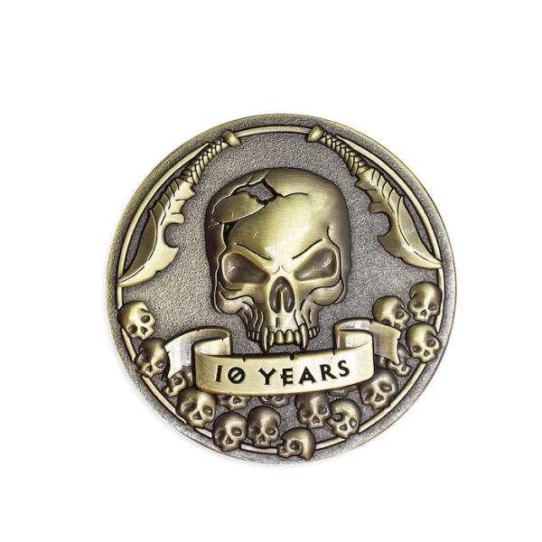A gold effect challenge coin featuring a 3D skull with two swords above its head and the words
