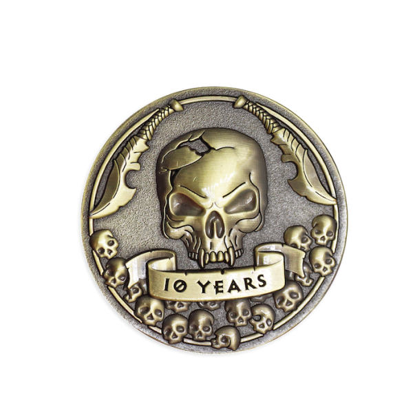 A gold effect challenge coin featuring a 3D skull with two swords above its head and the words
