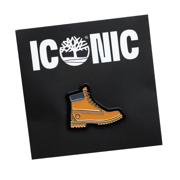 A pin badge in the shaped of a Timberland boot pinned to a black backing card that says