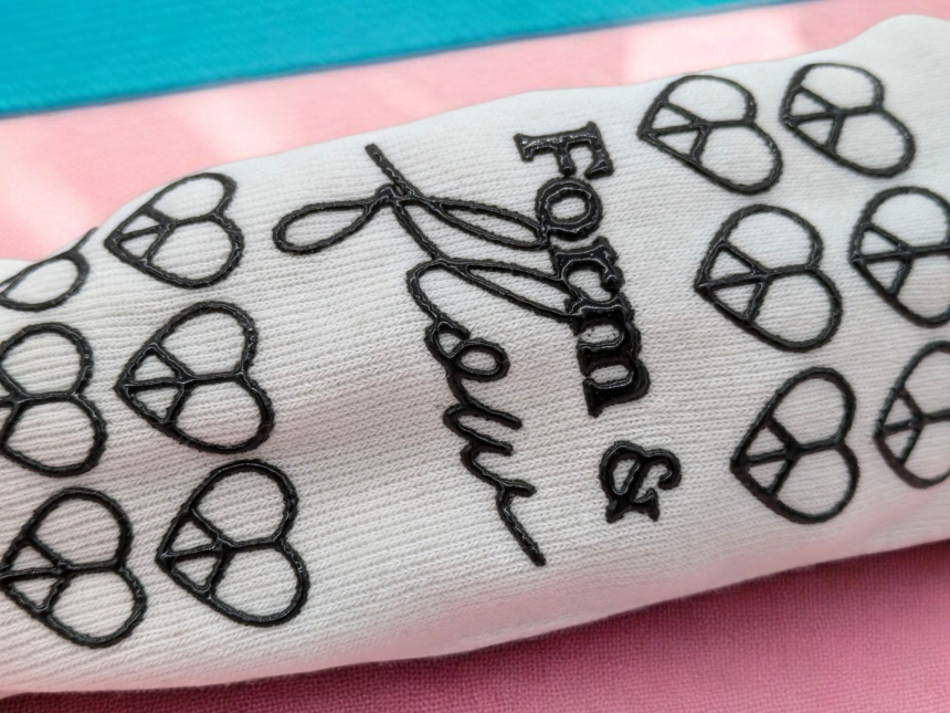 A white pilates sock with a black patterned grip on the sole. The pattern is hearts with the words 