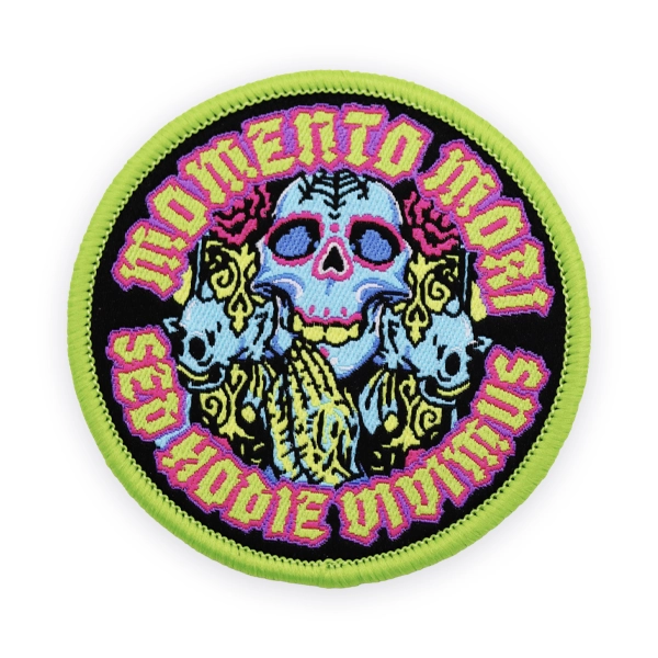Round woven patch featuring a colourful skull illustration and “Momento Mori Sod Noobie Uvinnings” text, produced as a vibrant custom woven patch with fine detail for clothing and accessories.